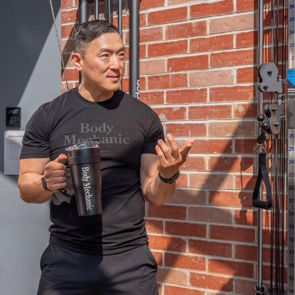 Man holding a 'Body Mechanic' tumbler against a brick wall