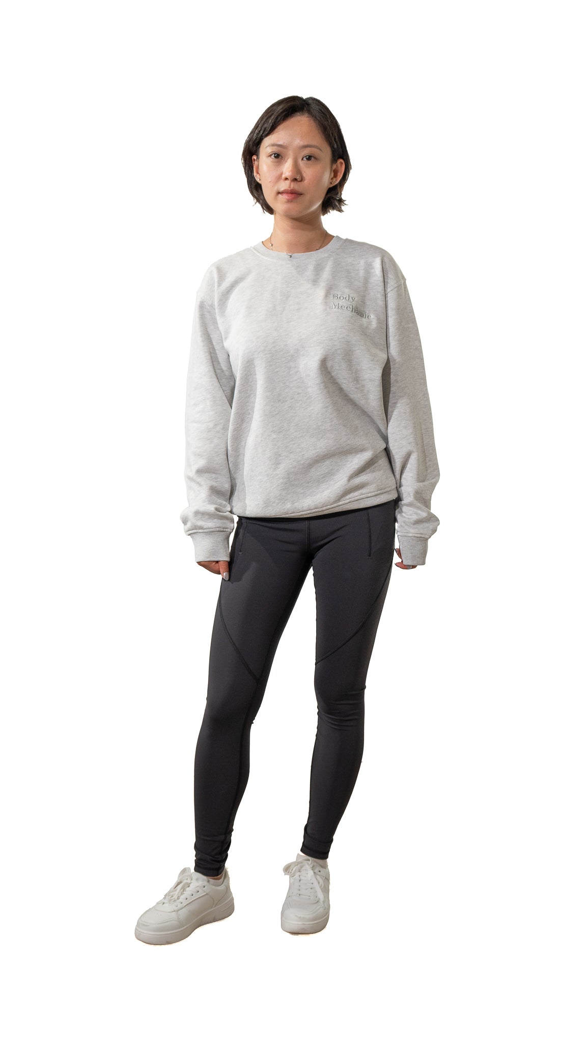 Person wearing a light gray sweatshirt, dark gray leggings, and white sneakers on a white background