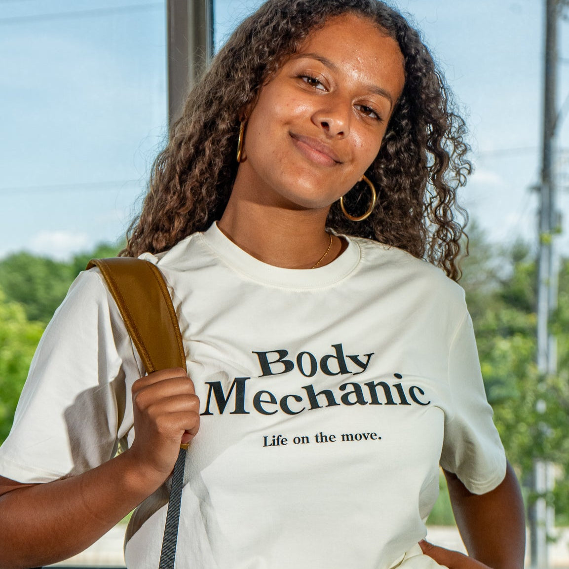 Person wearing a white t-shirt with 'Body Mechanic' text, standing outdoors.