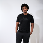 Man wearing a black t-shirt with text and black pants against a white wall.