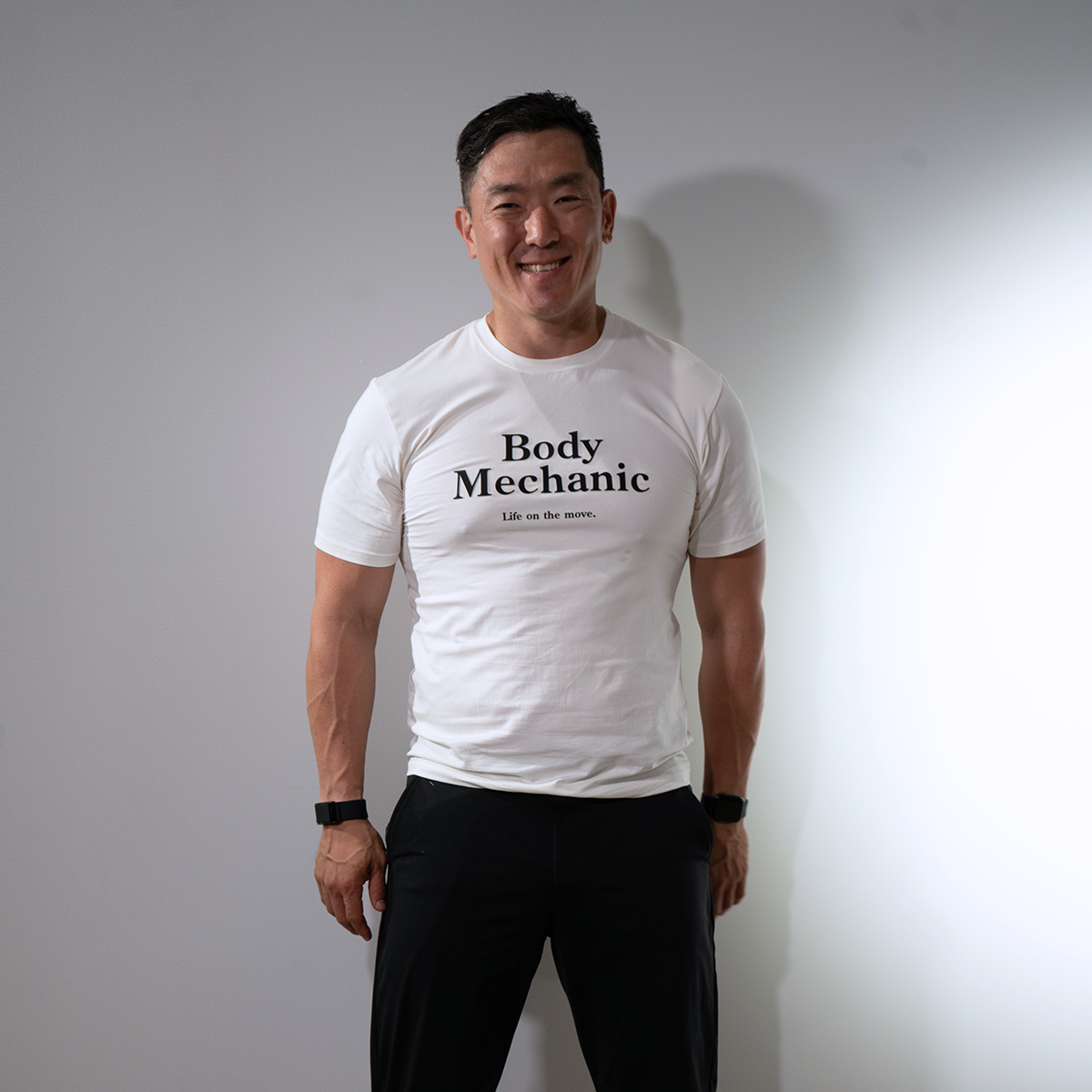Man wearing a white t-shirt with 'Body Mechanic' text against a plain background