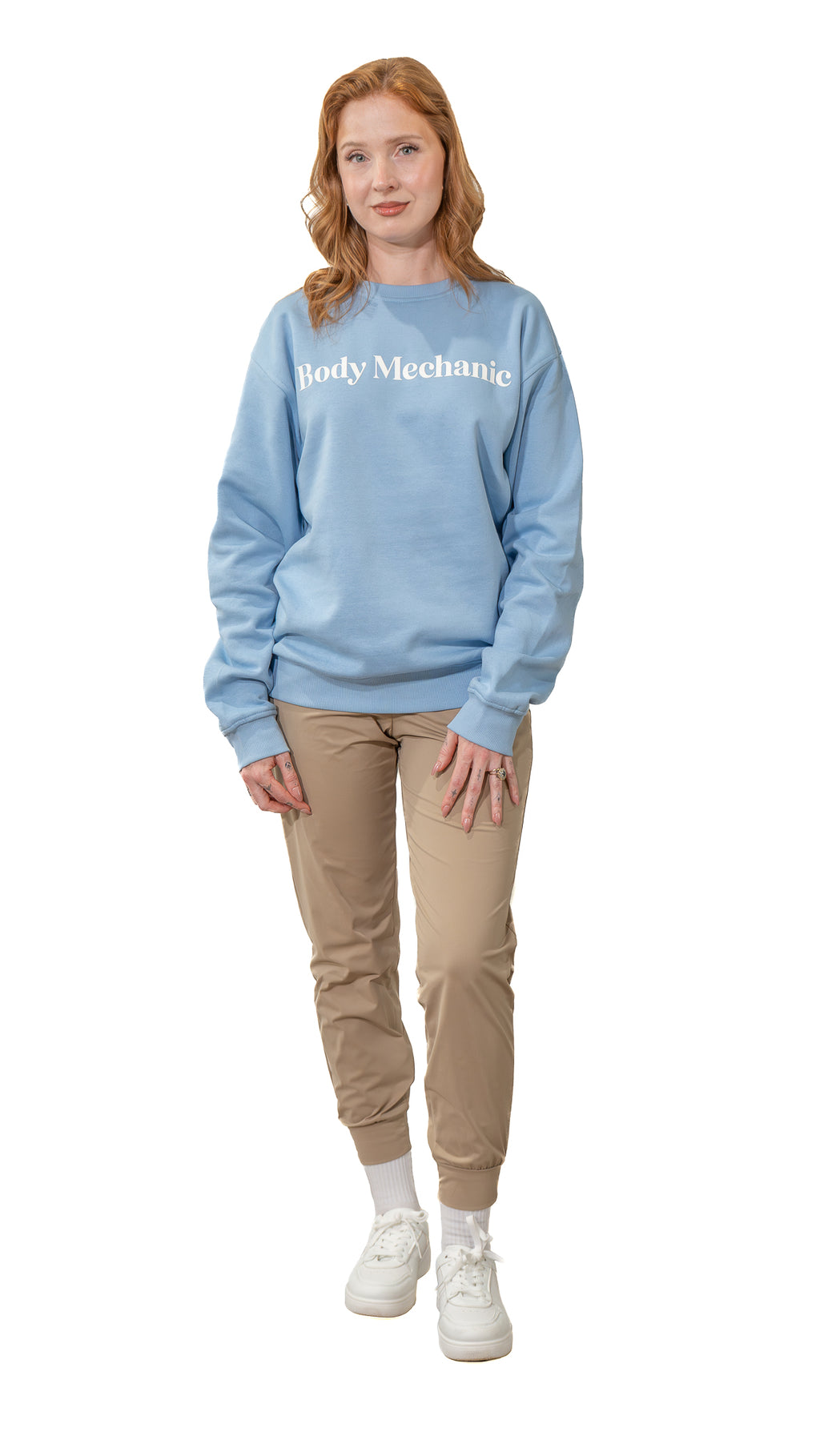 Woman wearing a light blue sweatshirt with text, beige pants, and white sneakers on a white background