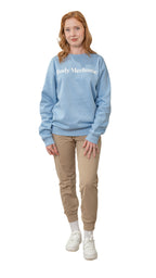 Woman wearing a light blue sweatshirt with text, beige pants, and white sneakers on a white background