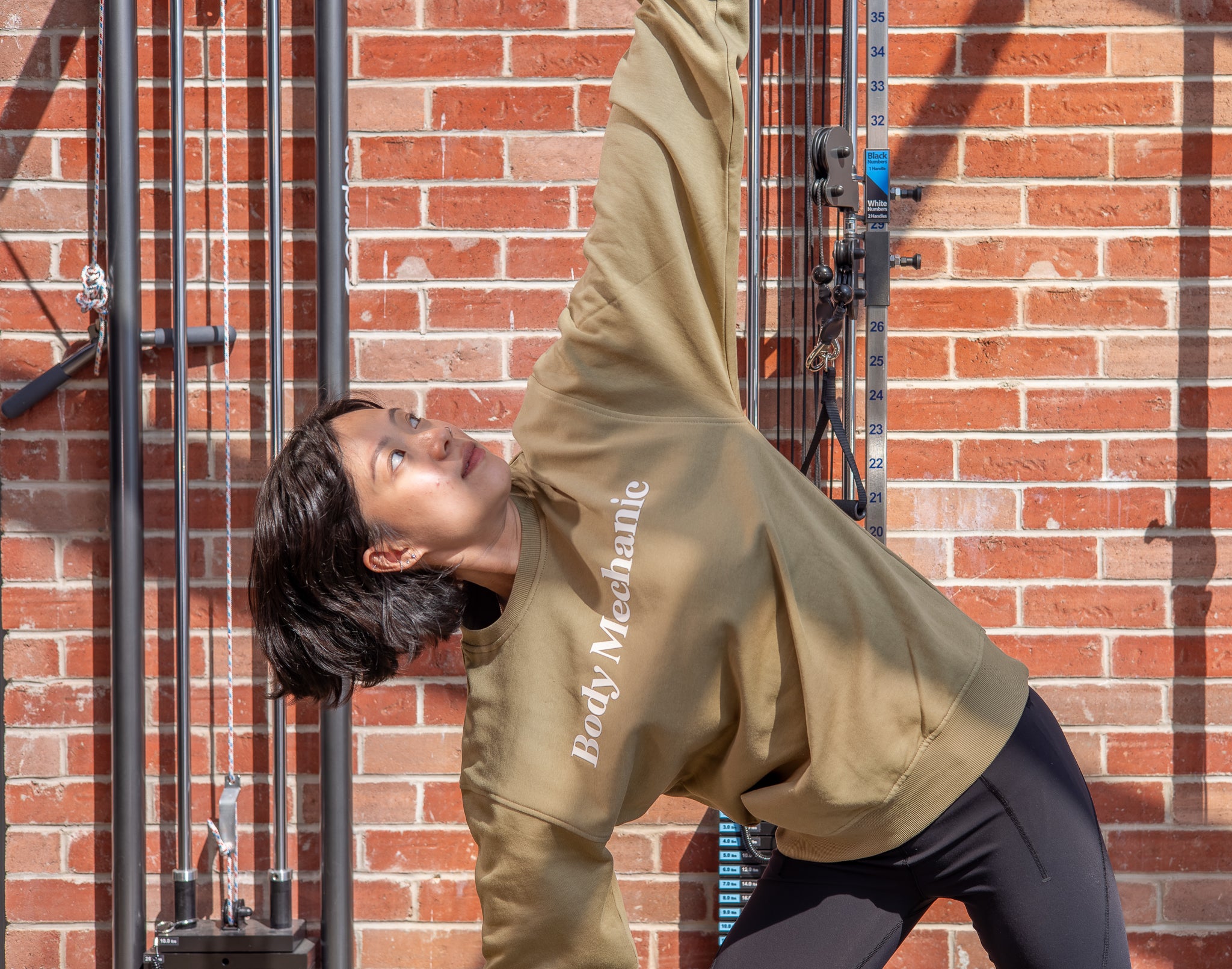 Person wearing a beige hoodie with 'Body Mechanic' text, in a yoga pose