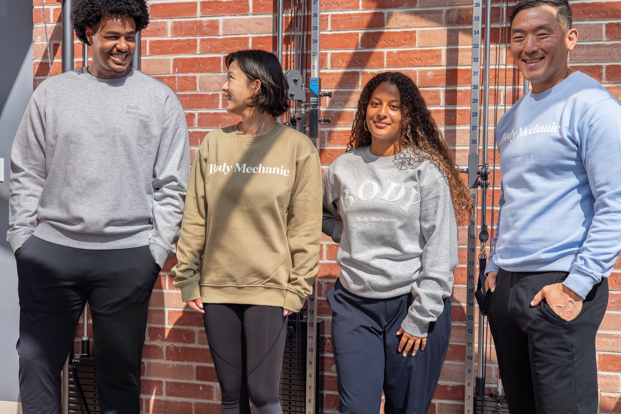 Four people wearing sweatshirts with visible branding in front of a brick wall.