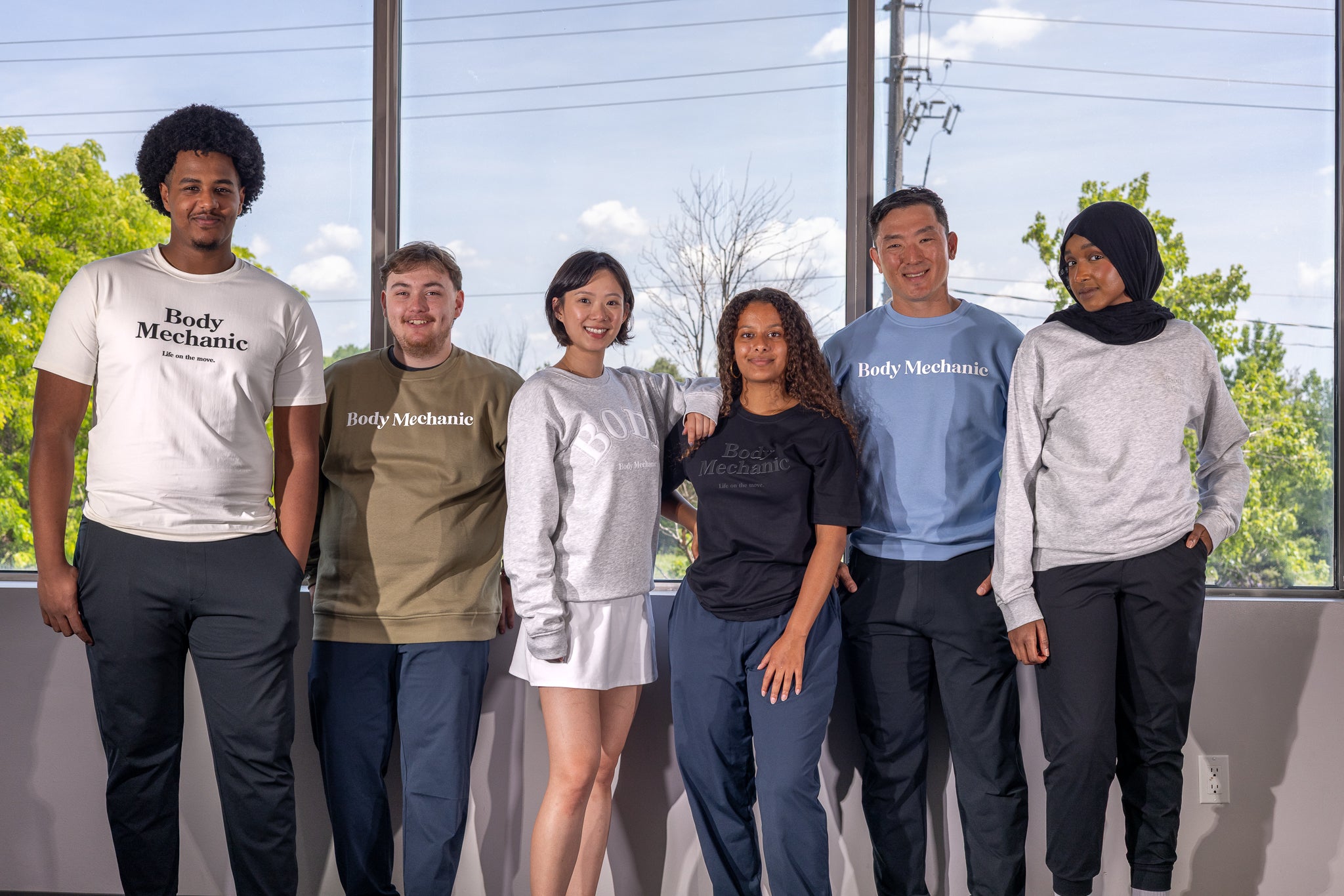 Group of six people wearing 'Body Mechanic' branded clothing standing outdoors.
