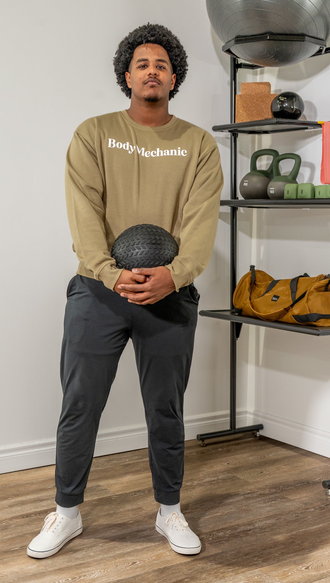 Man wearing a beige sweatshirt with 'BodyMechanic' text in a gym setting