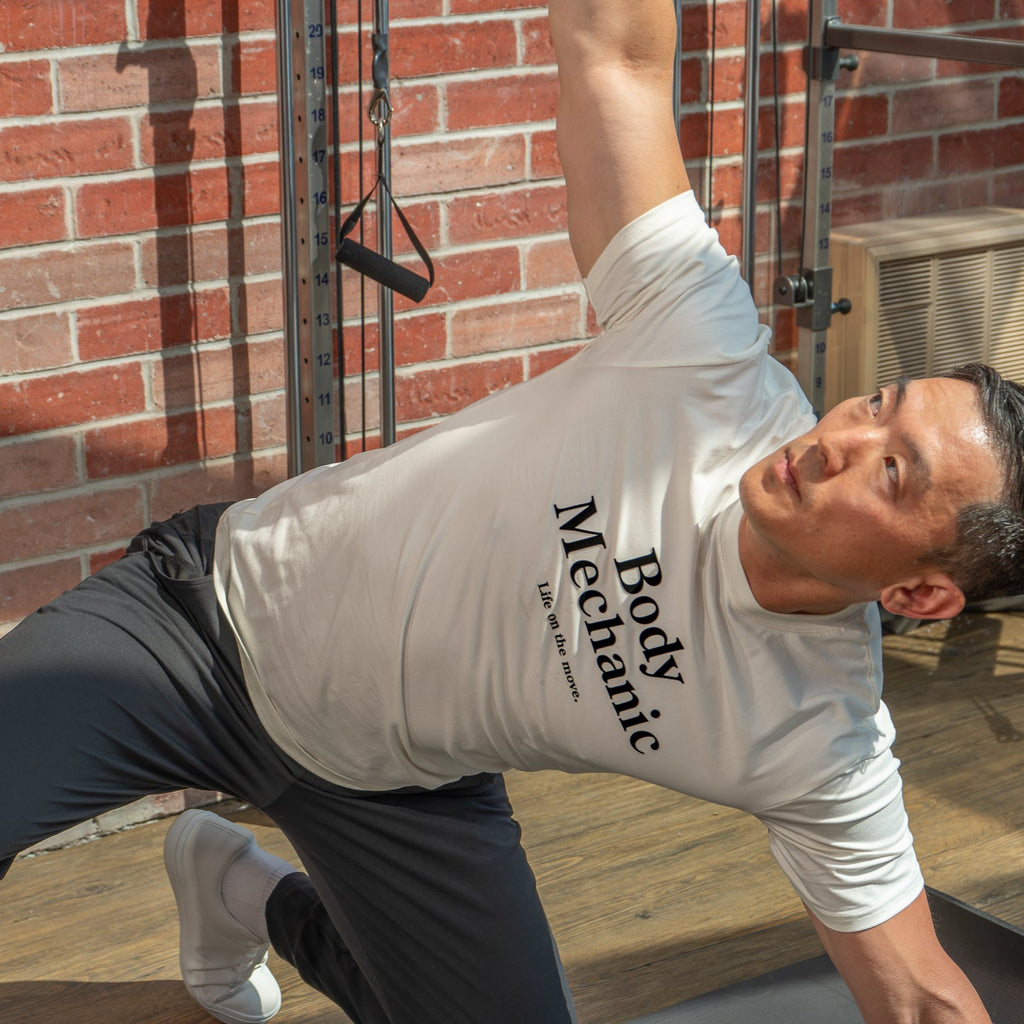Man exercising outdoors wearing a 'Body Mechanic' t-shirt against a brick wall.