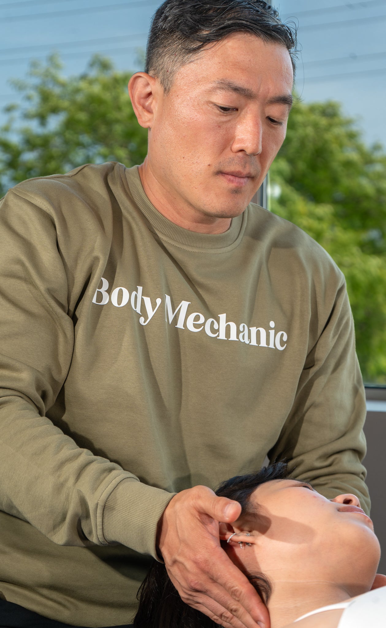 Person wearing a 'Body Mechanic' sweatshirt attending to a client in a clinical setting.